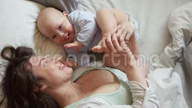 可爱的母亲在她的小男孩躺在一张白色的床上挠痒痒。 软焦